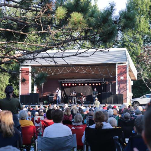 A band performing on outdoor bandstand with huge crowd
