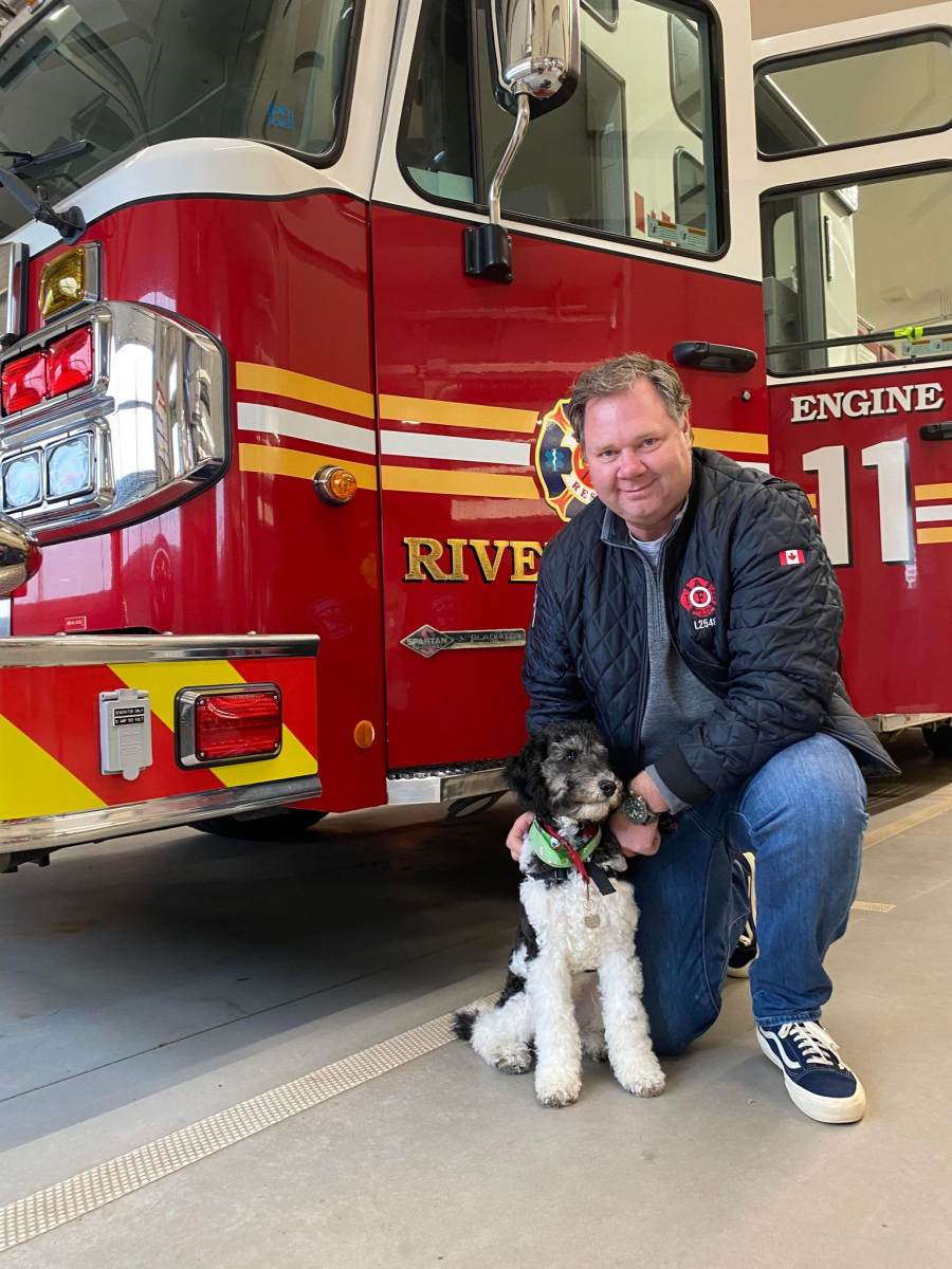 Facility dog sits next to fire truck with Dave Murray