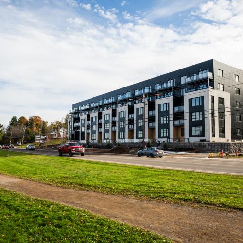 two people walk on riverfront trail with apartment in background