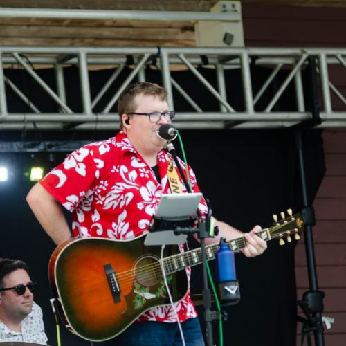 A man in red and white shirt with guitar performing