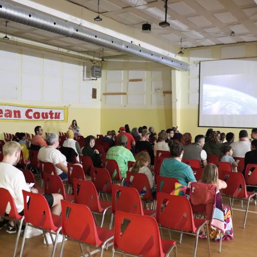A crowd of people in chairs watching a movie on a screen