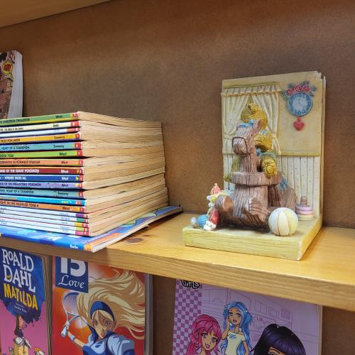 A stack of colorful children's books and a wooden animal decor item on a bookshelf.