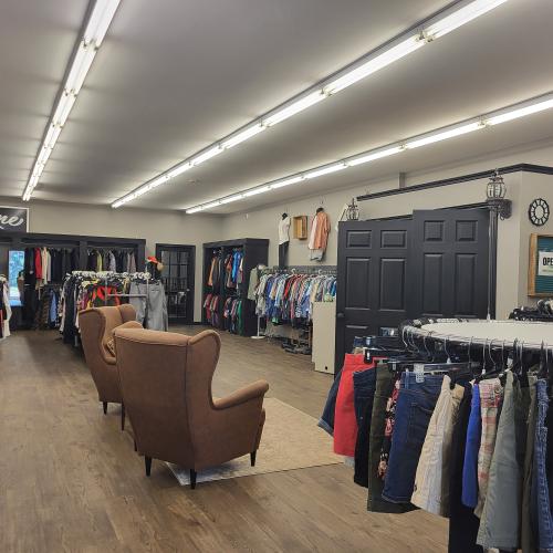 Racks of clothing inside the thrift store. A small waiting area with 2 brown, cushioned chairs beside the fitting rooms.