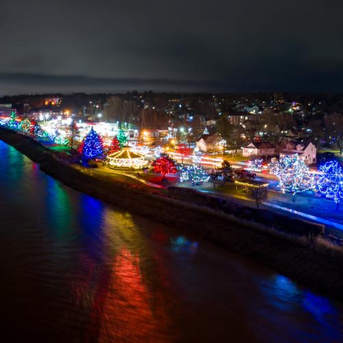 Aerial view of christmas lights on trees along a riverbank 