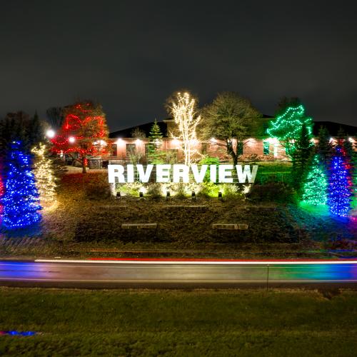 A sign reading RIVERVIEW lit up with christmas lights all around