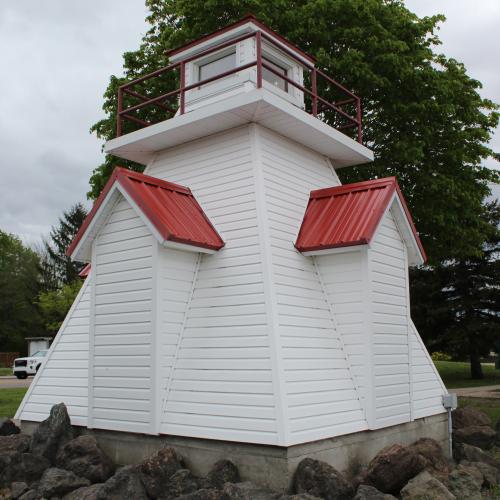 White lighthouse with red roofing surrounded by stones. The background shows trees.