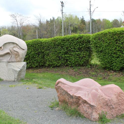 2 stone sculptures next the gravel path surrounded by grass and bushes
