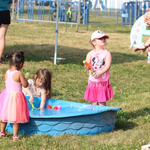 Three children playing with water toys in a plastic pool at a park