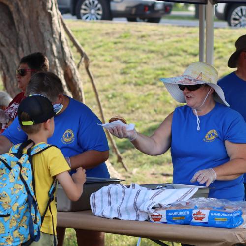A woman in a blue shirt handing a hamburger to a boy 