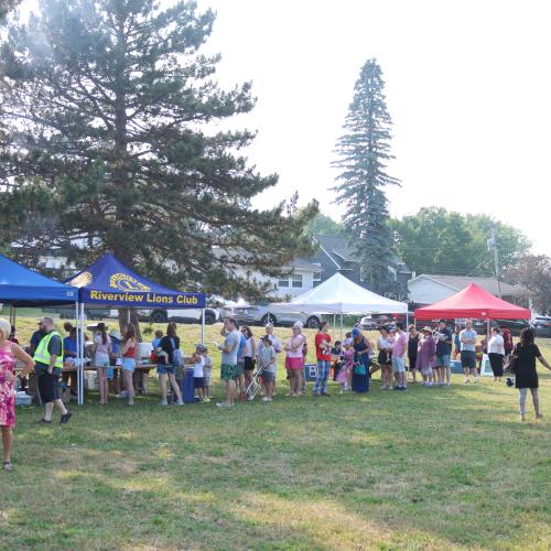 Tents and people lined up at a park on a sunny day 