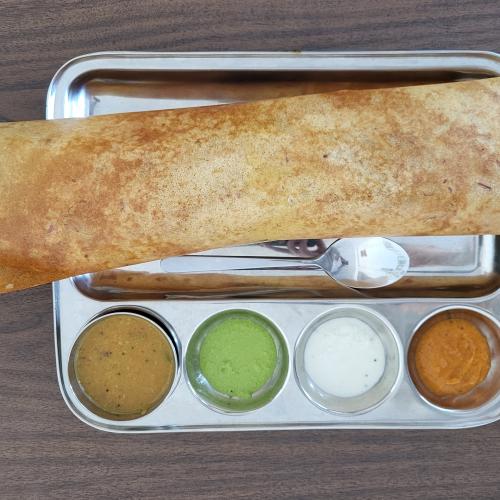 A dosa layed on a metal plate seved with 3 sauces and a soup