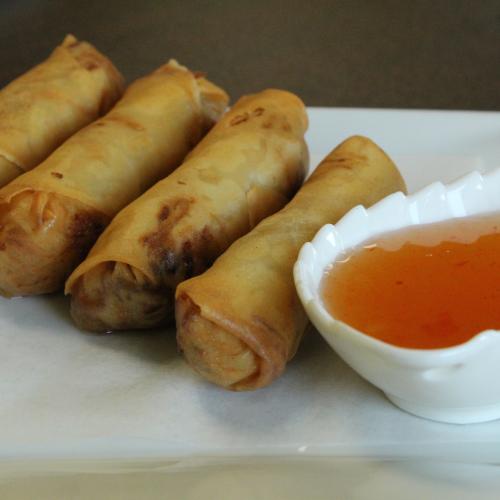4 spring rolls on asquare white plate with an orage sauce on the side