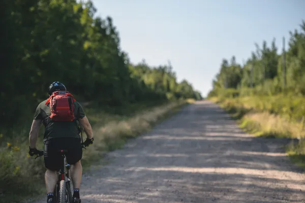 man biking on gravel trail with red bookbag