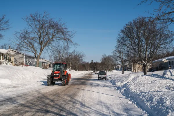 Orange snowplow driving down a snowy neighbourhood street