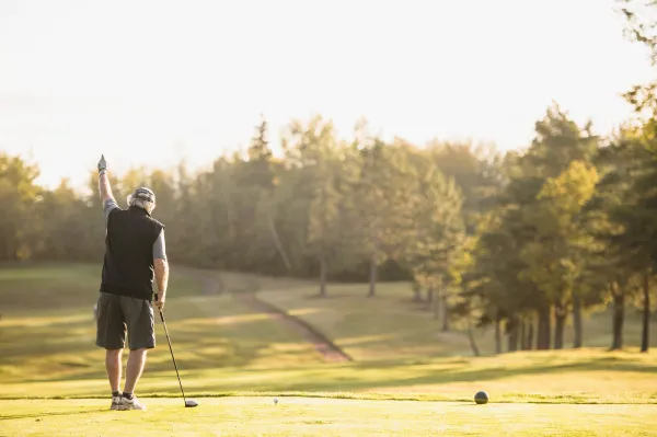 Older man waves at sunrise at golf course
