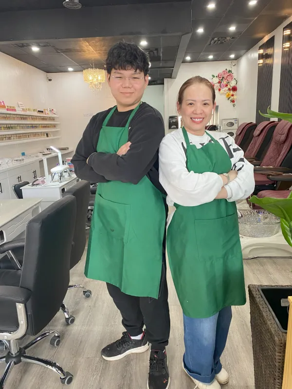 A woman and a man standing back to back with arms crossed in a nail salon