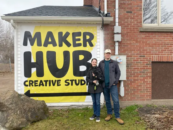 A smiling couple with their yorki in front of Maker Hub sign