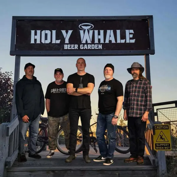 Band members standing in front of the Holy Whale garden sign.