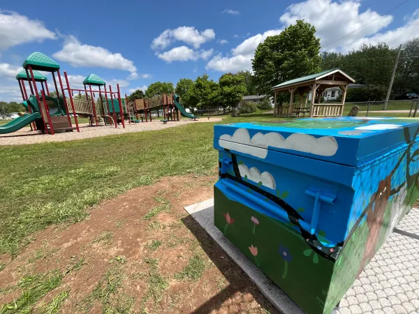 Play structure, painted play box full of toys and picnic structure on a blue sky day.