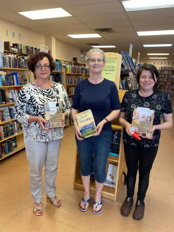 Crystal at Cover to Cover standing with her coworkers, smiling and holding books