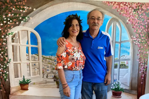 A man and woman smiling in front of a mural of santorini