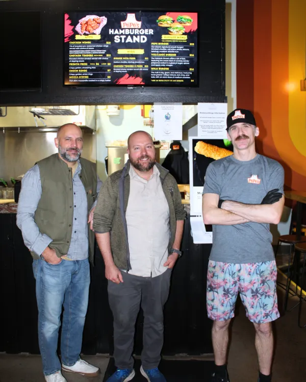 Three men standing by an indoor restaurant smiling