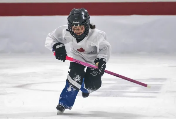 Young person skating with a ringette stick.
