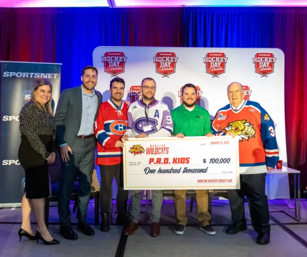 Group of people smiling and holding a large ceremonial cheque at a presentation event.