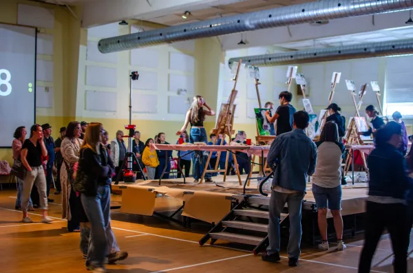 Youth participating in a live painting competition surrounded by an audience. 
