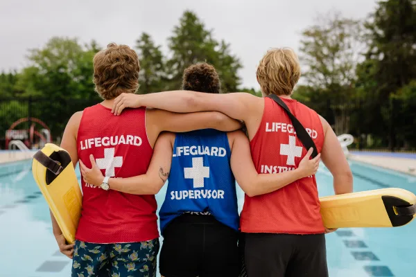 Three lifeguards standing poolside, facing the swimming pool.