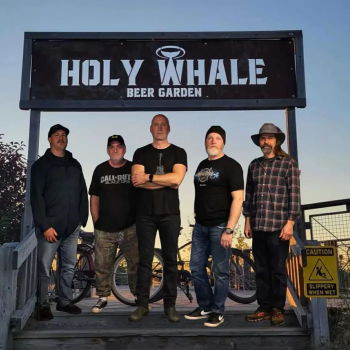 Band members standing in front of the Holy Whale garden sign.