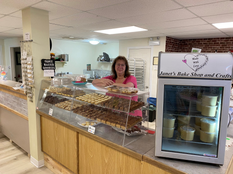 Janet inside her bakery standing behind the display case