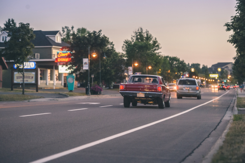 rear view of a red vintage car driving down a street at dusk, business lights in the background