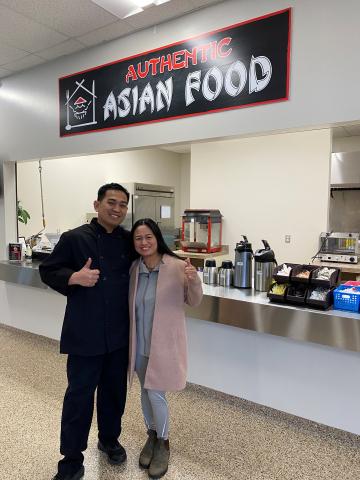 male and female owners give a thumbs up in front of authenic asian food canteen