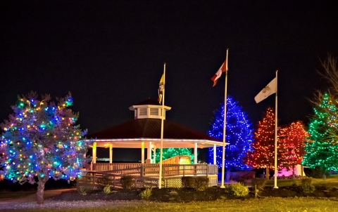 Riverfront trail gazebo and trees illuminated with holiday lights