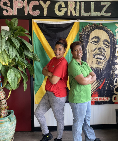 Two women stand in front of Jamaican flag and bob marley poster at restaurant