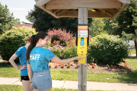 Two women using an automatic sunscreen dispenser outside