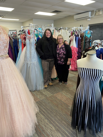 Business owners Annie and Joanne stand inside store surrounded by prom dresses