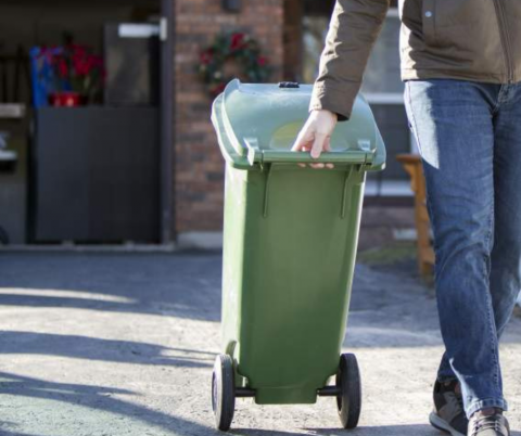 Man rolls green garbage bin to the curb