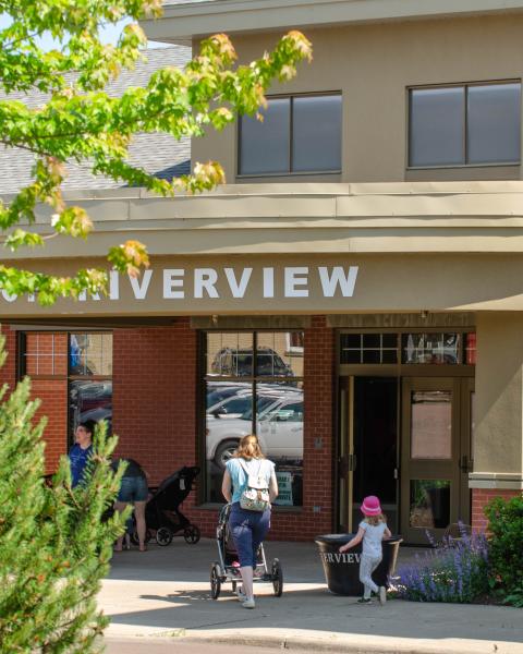 A mother pushing a stroller into the library on a summer day with another child walking beside them
