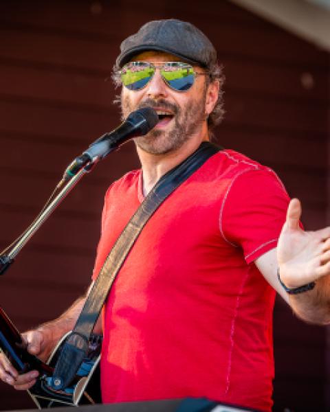 Singer in a red shirt and sunglasses singing into microphone