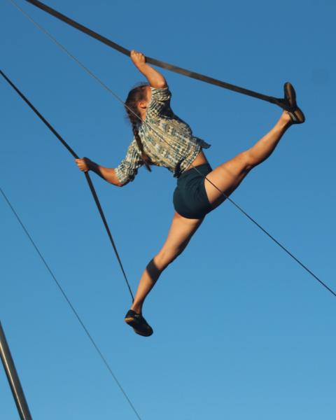 A woman suspended in the air doing acrobatics outside
