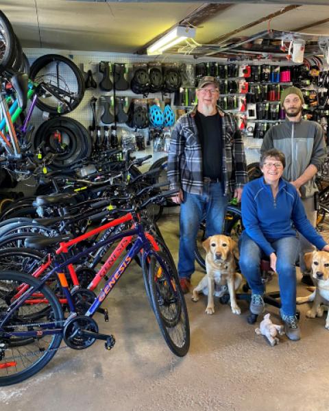 3 people and 2 golden labs standing inside a bike shop