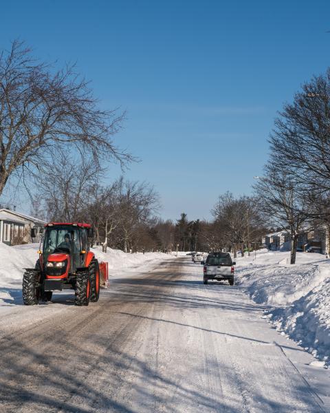 Orange snowplow driving down a snowy neighbourhood street