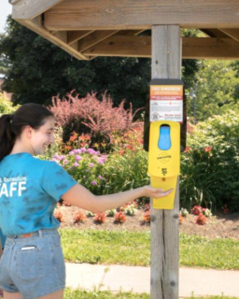 Two people using outdoor sunscreen dispenser