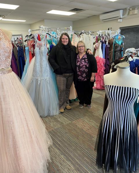 Business owners Annie and Joanne stand inside store surrounded by prom dresses