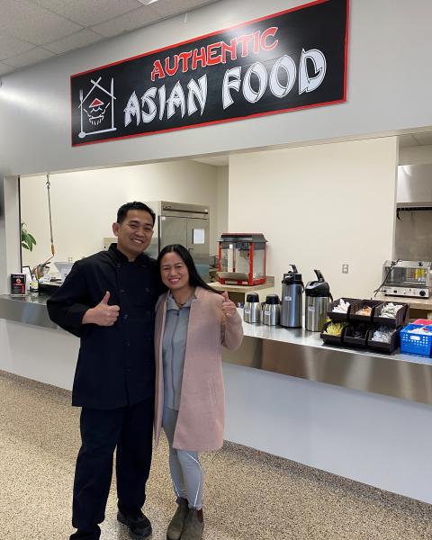 male and female owners give a thumbs up in front of authenic asian food canteen