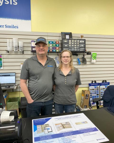 A husband and wife stand behind service counter smiling