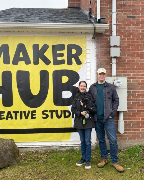 A smiling couple with their yorki in front of Maker Hub sign