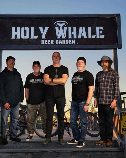 Band members standing in front of the Holy Whale garden sign.